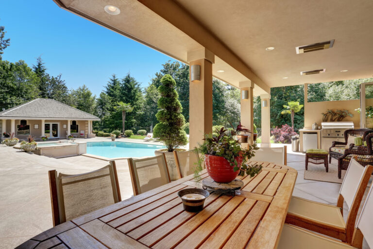 esterni di una casa in legno. si vedono una piscina, un gazebo, un tavolo in legno con 4 sedie e un vaso di margherite come centrotavola. il clima è soleggiato e fa pensare alla stagione estiva.